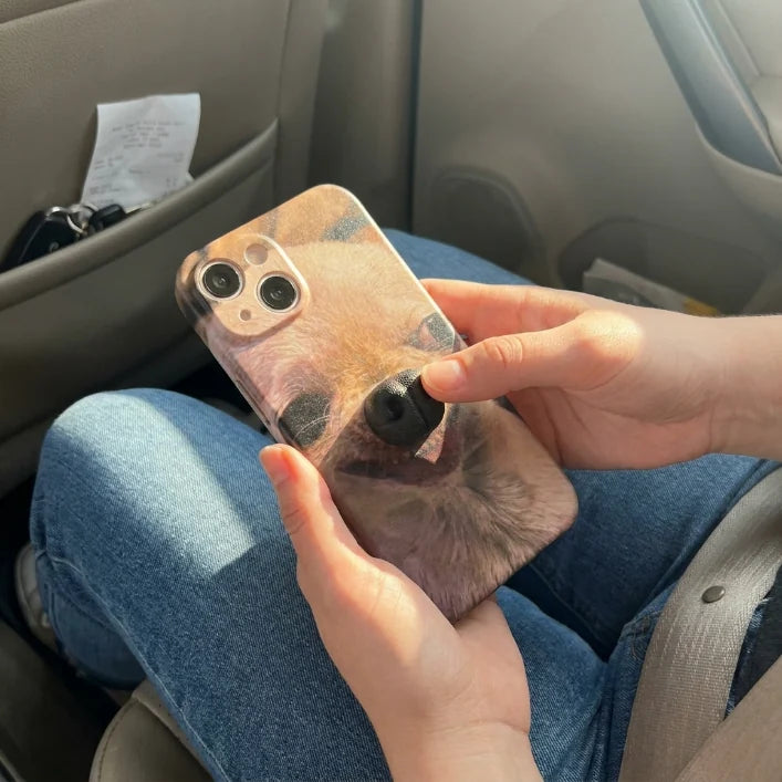 Hand pressing the 3D puppy nose on a BoopNose phone case in a car